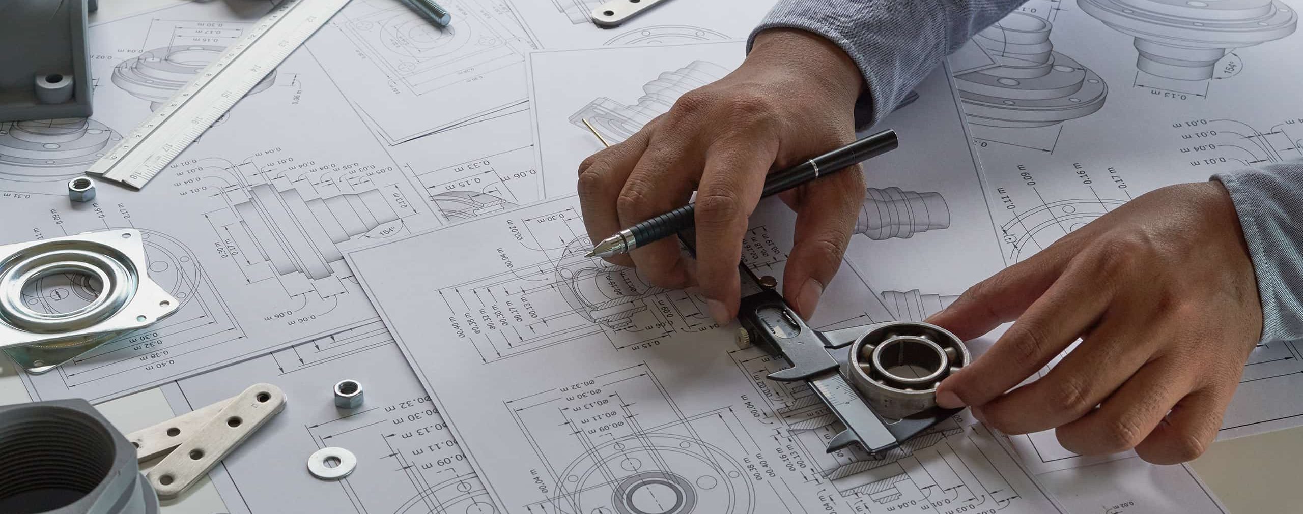 An engineer measuring a cylinder with a set of calipers while looking at drawings